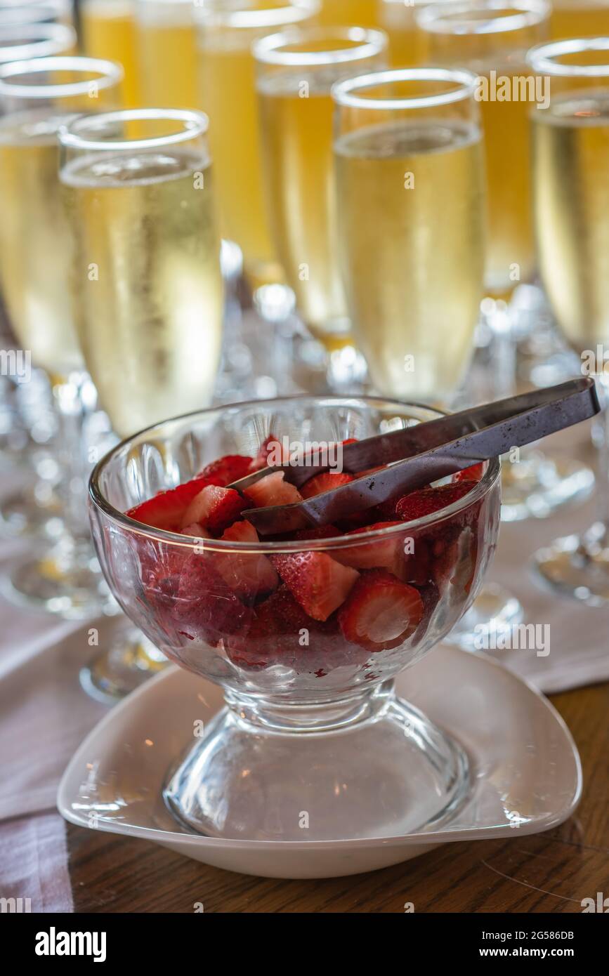 Fresh strawberries in a glass bowl with glasses of champagne blurred in the background. Stock Photo