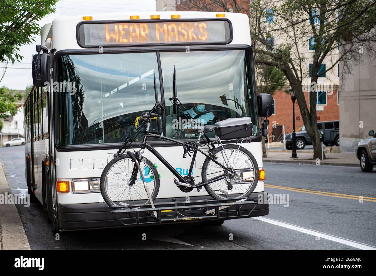 Public transportation bus with a sign that says WEAR MASKS and a bicycle on the front of the bus. Stock Photo