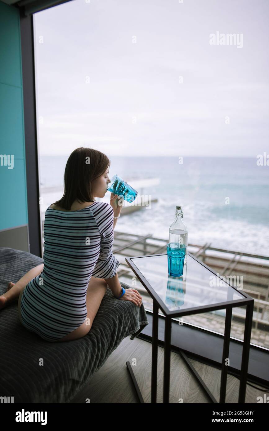 Rear view of woman drinking water in hotel with view on sea Stock Photo
