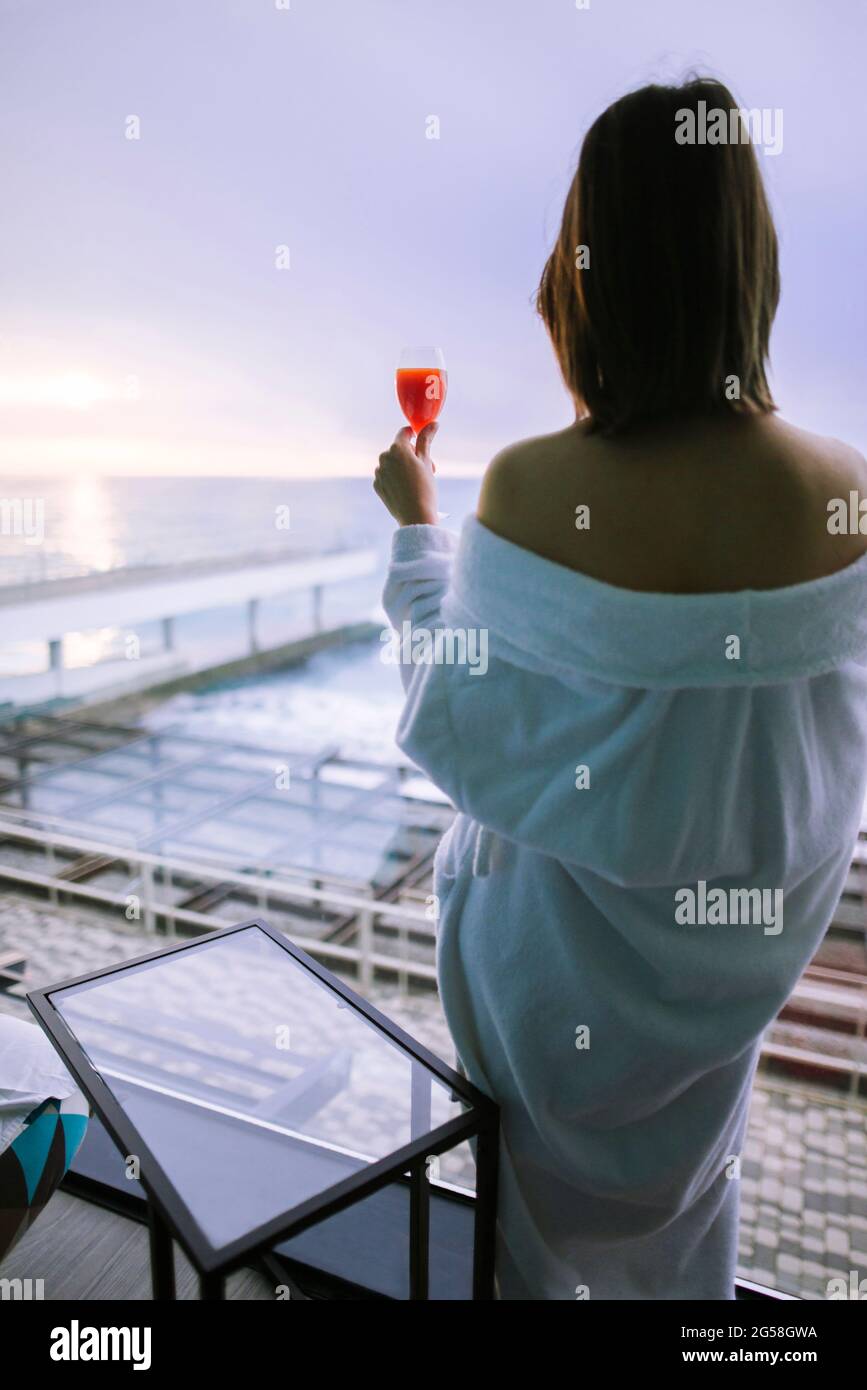 Rear view of woman with cocktail in hotel and observing sunrise over sea Stock Photo