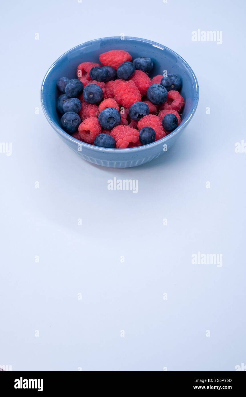 Vertical shot of fresh blueberries and raspberries in a bowl isolated ...