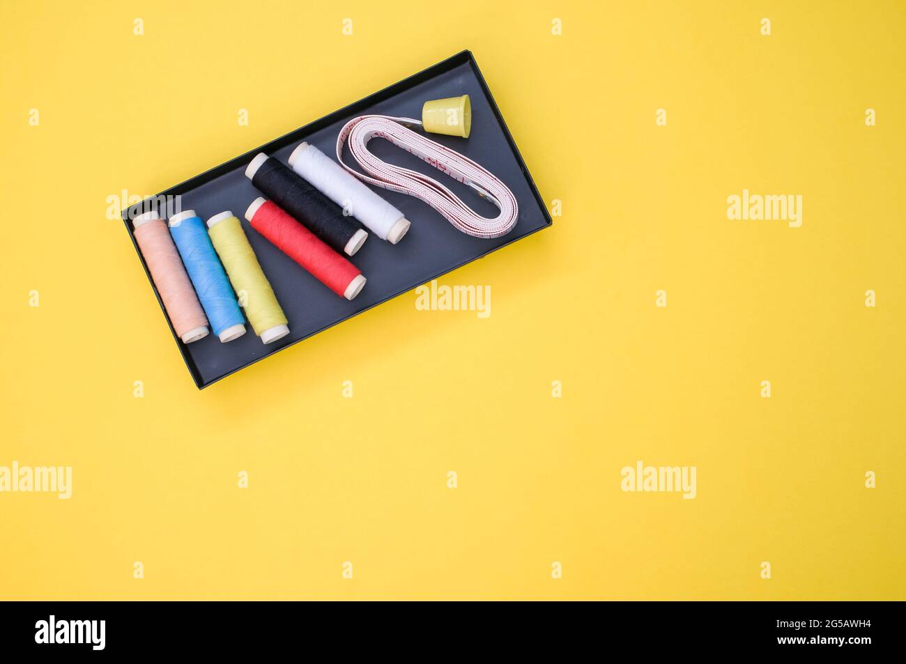 Pack of colorful sewing threads and a measuring tape on yellow ...