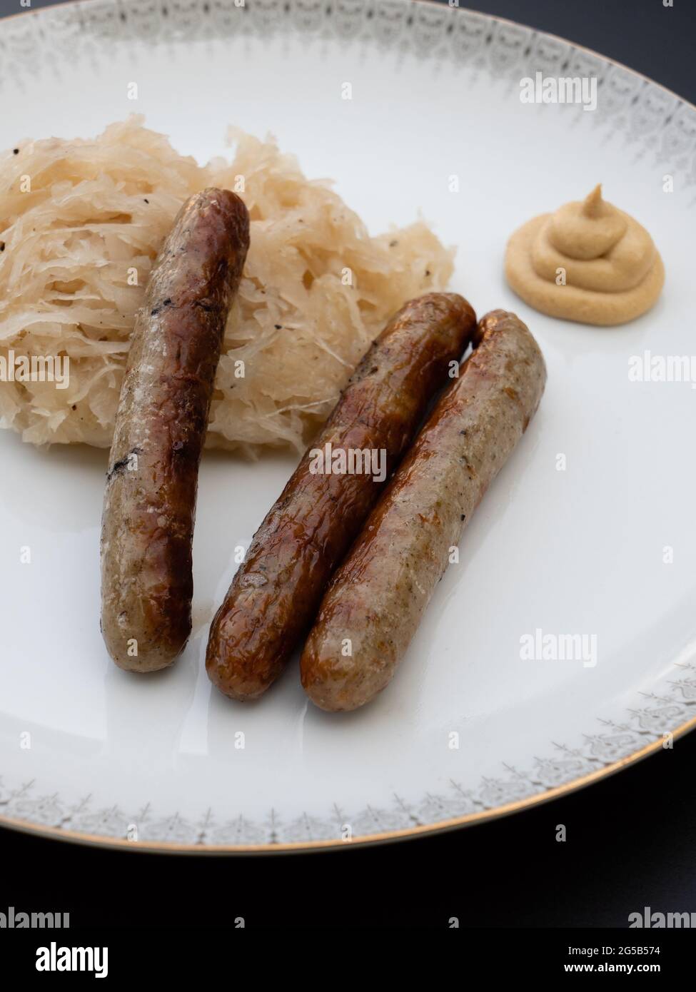 Nuremberg Grilled Sausage or Nürnberger Rostbratwurst with Sauerkraut or Sour Cabbage and Mustard on a White Plate Vertical Orientation Stock Photo