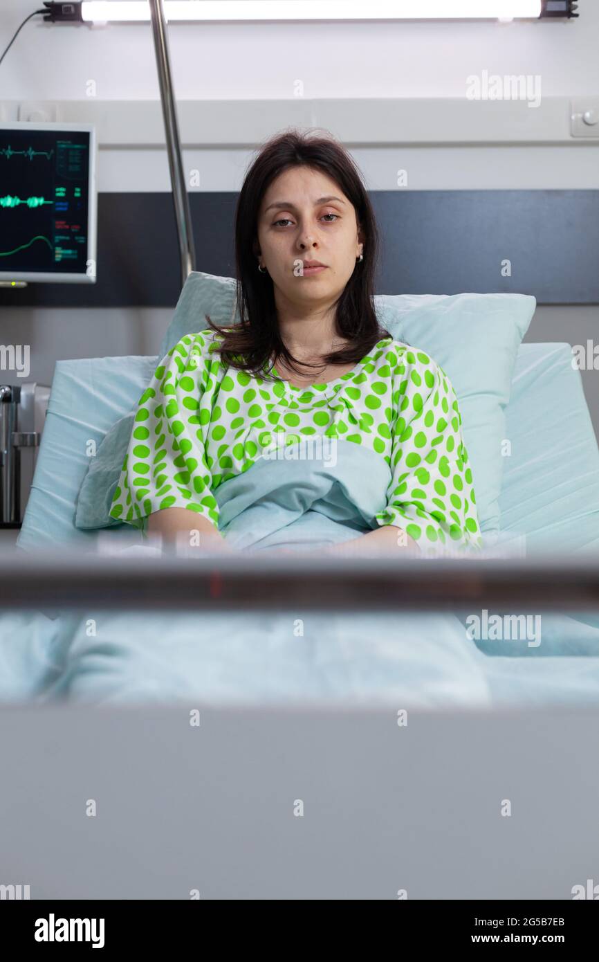 Sick woman wearing with nasal oxygen tube looking into camera resting in bed recovering after respiratory disorder. Patient with breathing disease waiting for illness treatment in hospital ward Stock Photo