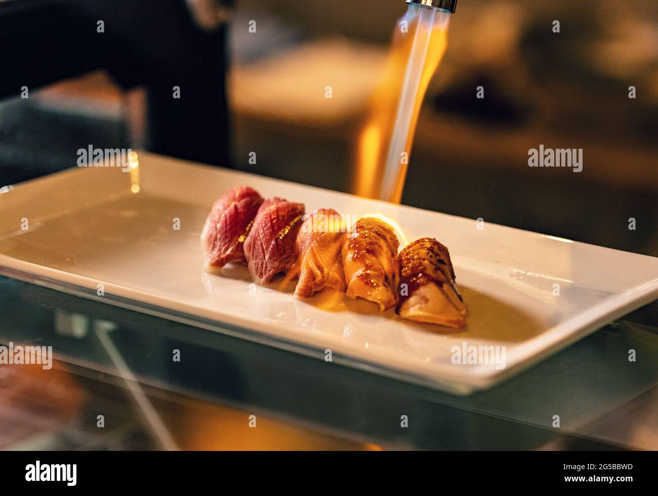 Close up hand of chef using kitchen torch burn on salmon sushi, japanese cuisine. Stock Photo