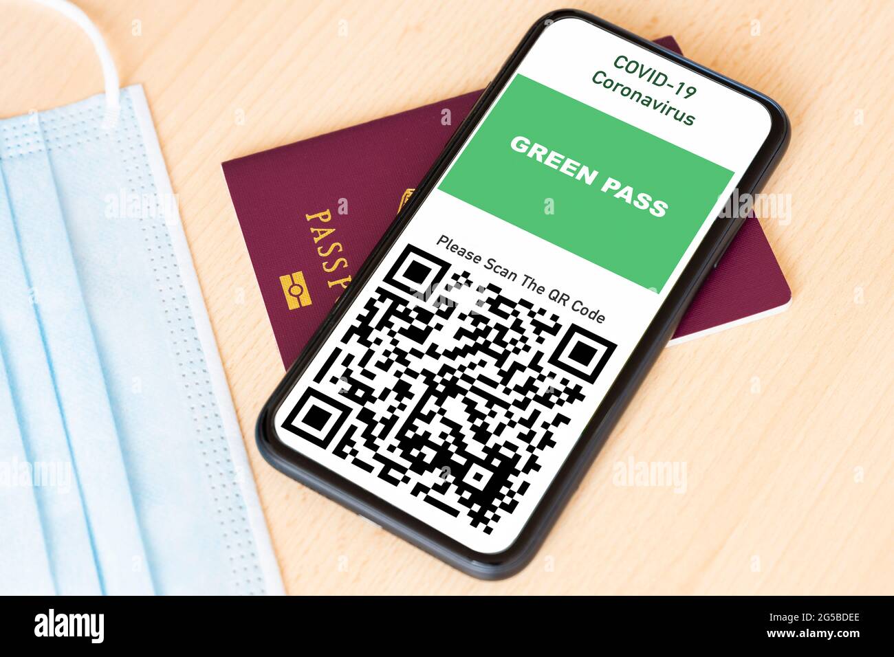 A passport and a smartphone with a Green Pass are arranged on a wooden table. Stock Photo