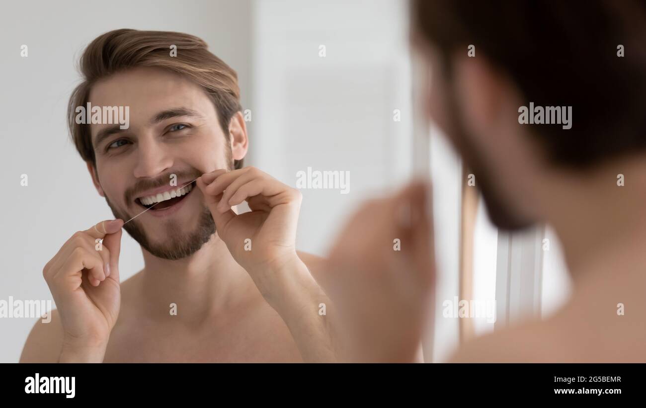 Happy handsome young guy cleaning white teeth with floss Stock Photo