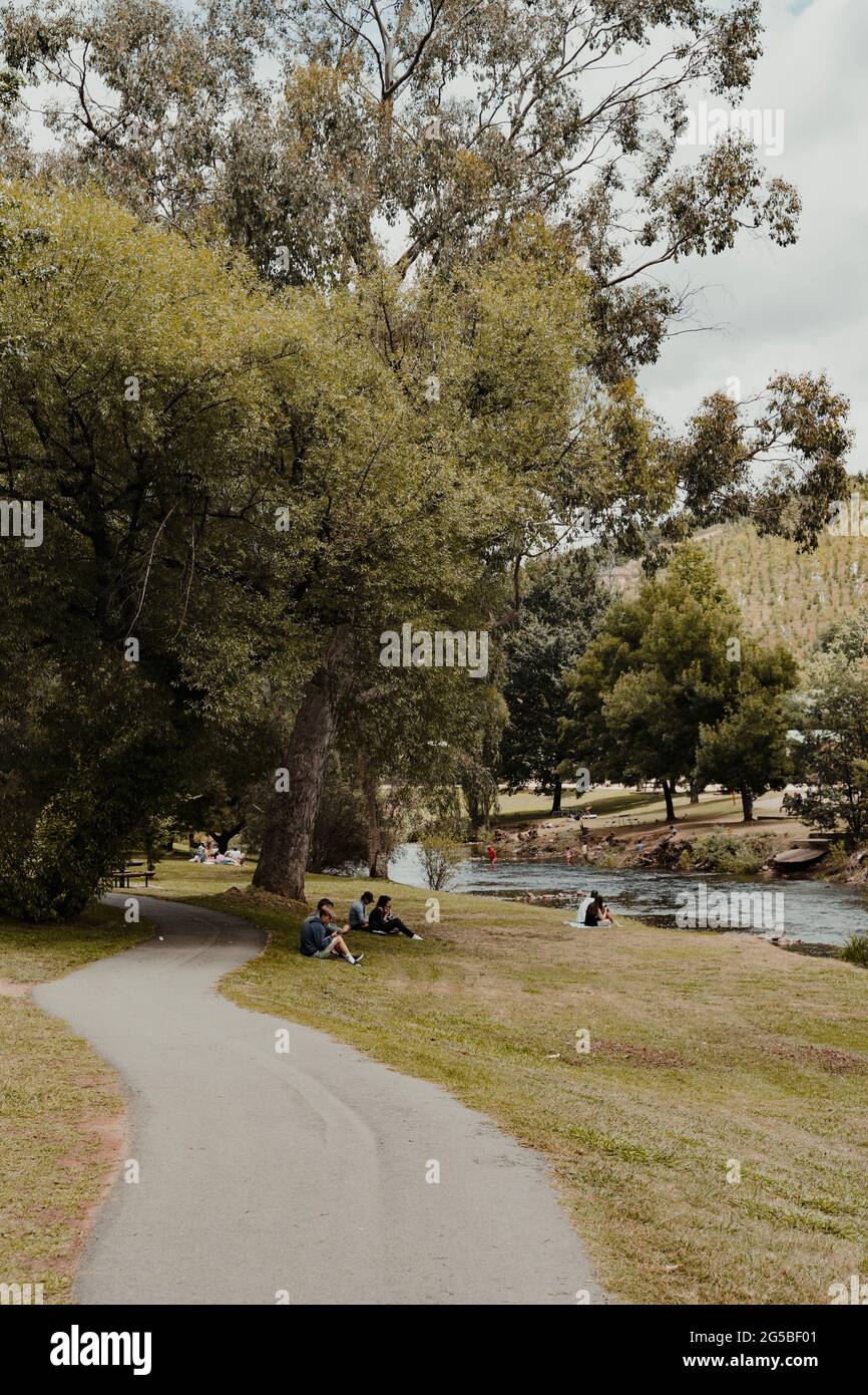 People relaxing alongside the Ovens River at Howitt Park, Bright VIC. Bright, Victoria - December 22nd, 2020 Stock Photo