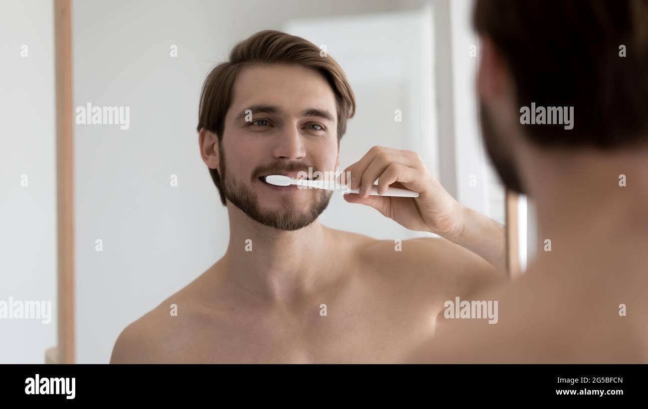 Positive handsome well built guy brushing teeth in bathroom Stock Photo