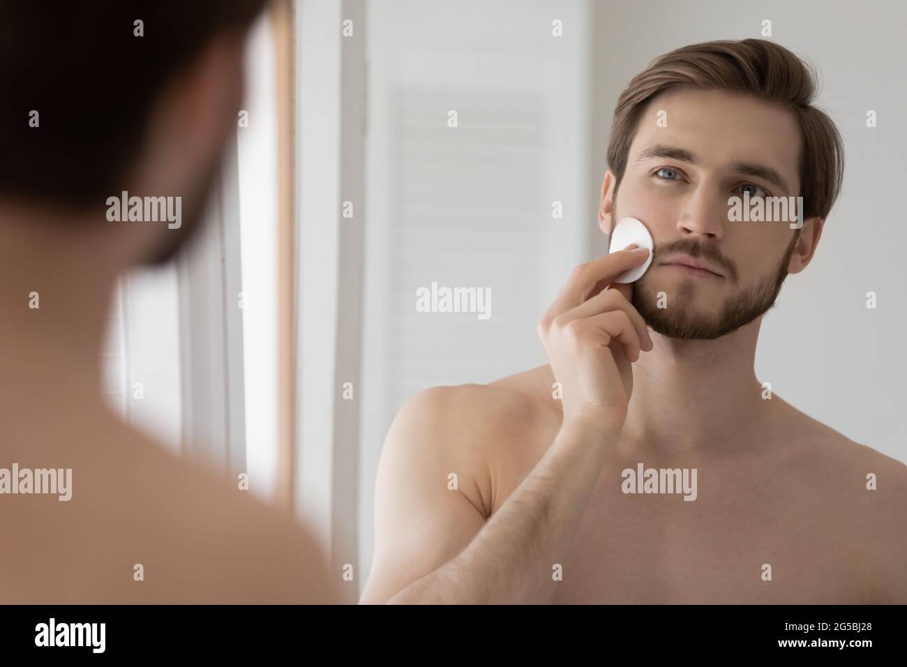 Attractive metrosexual guy cleansing face with cotton disc Stock Photo