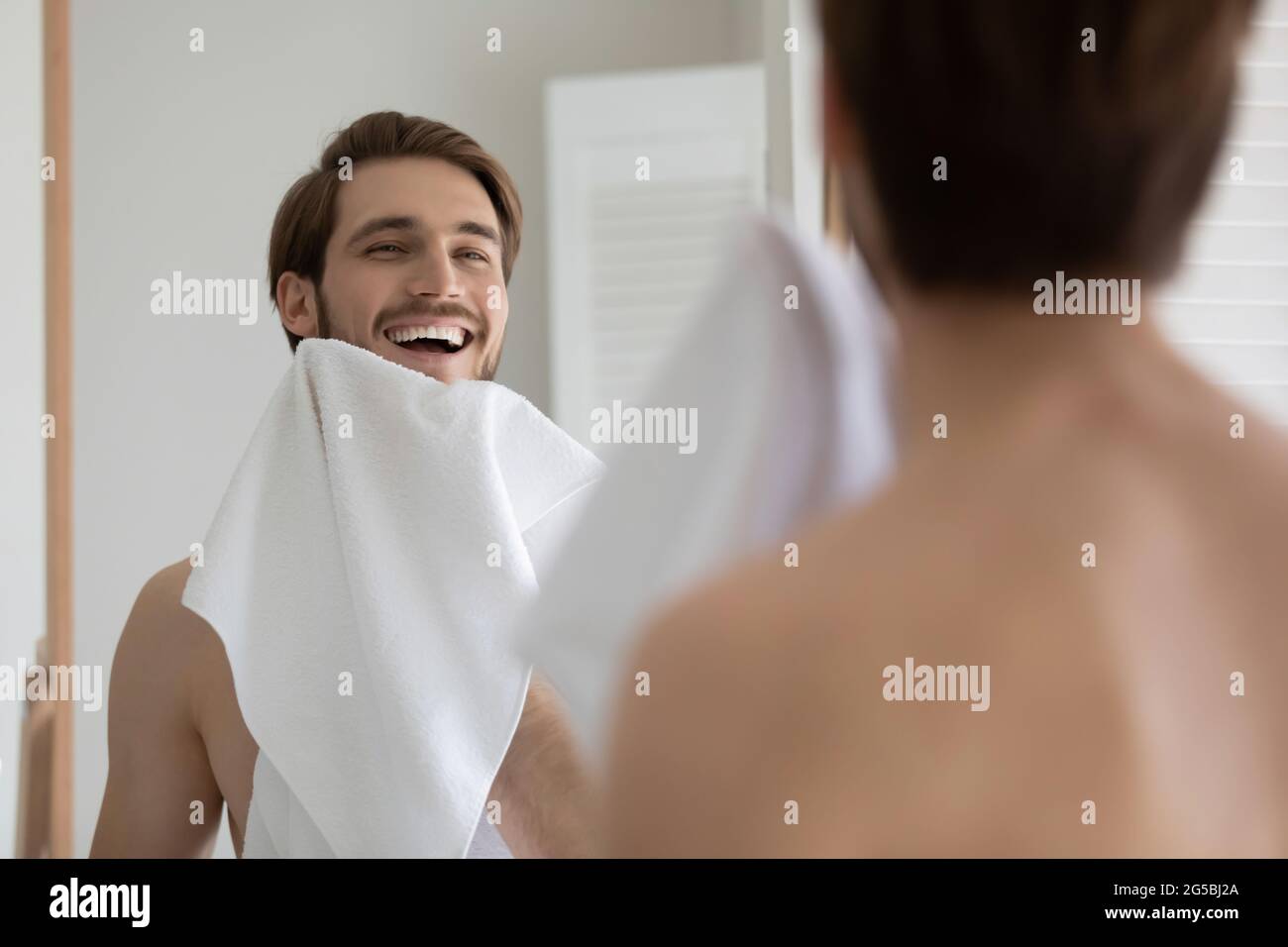 Happy attractive young millennial guy drying beard with white towel Stock Photo