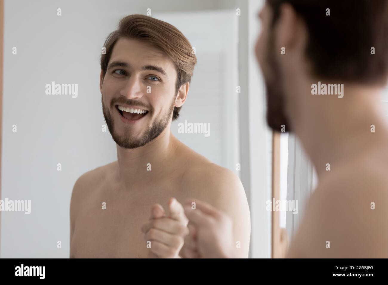 Happy guy having fun at mirror during daily bath procedures Stock Photo