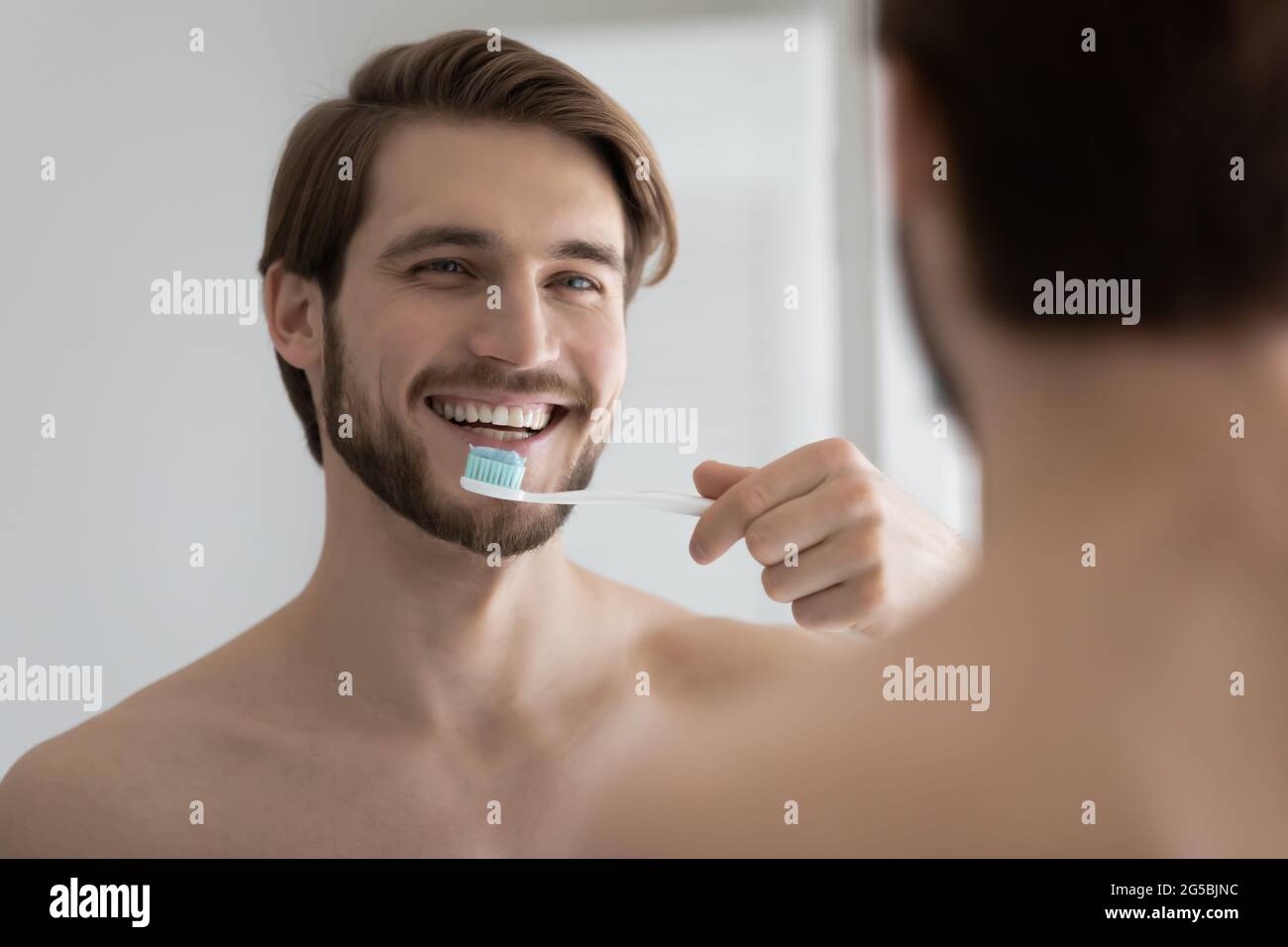 Happy attractive young man brushing healthy teeth in bathroom Stock Photo