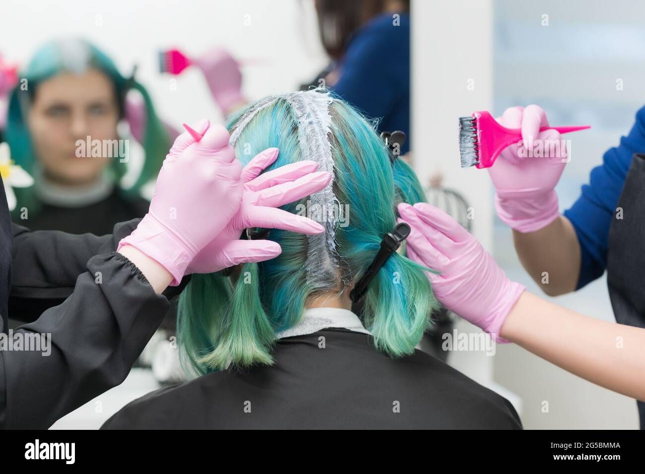 Two professional master hairdressers apply paint to woman hair during