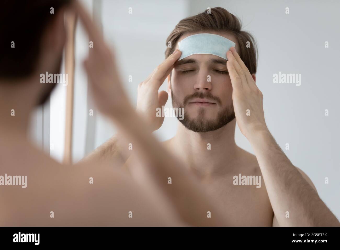 Calm metrosexual millennial man applying cleansing patch on forehead Stock Photo