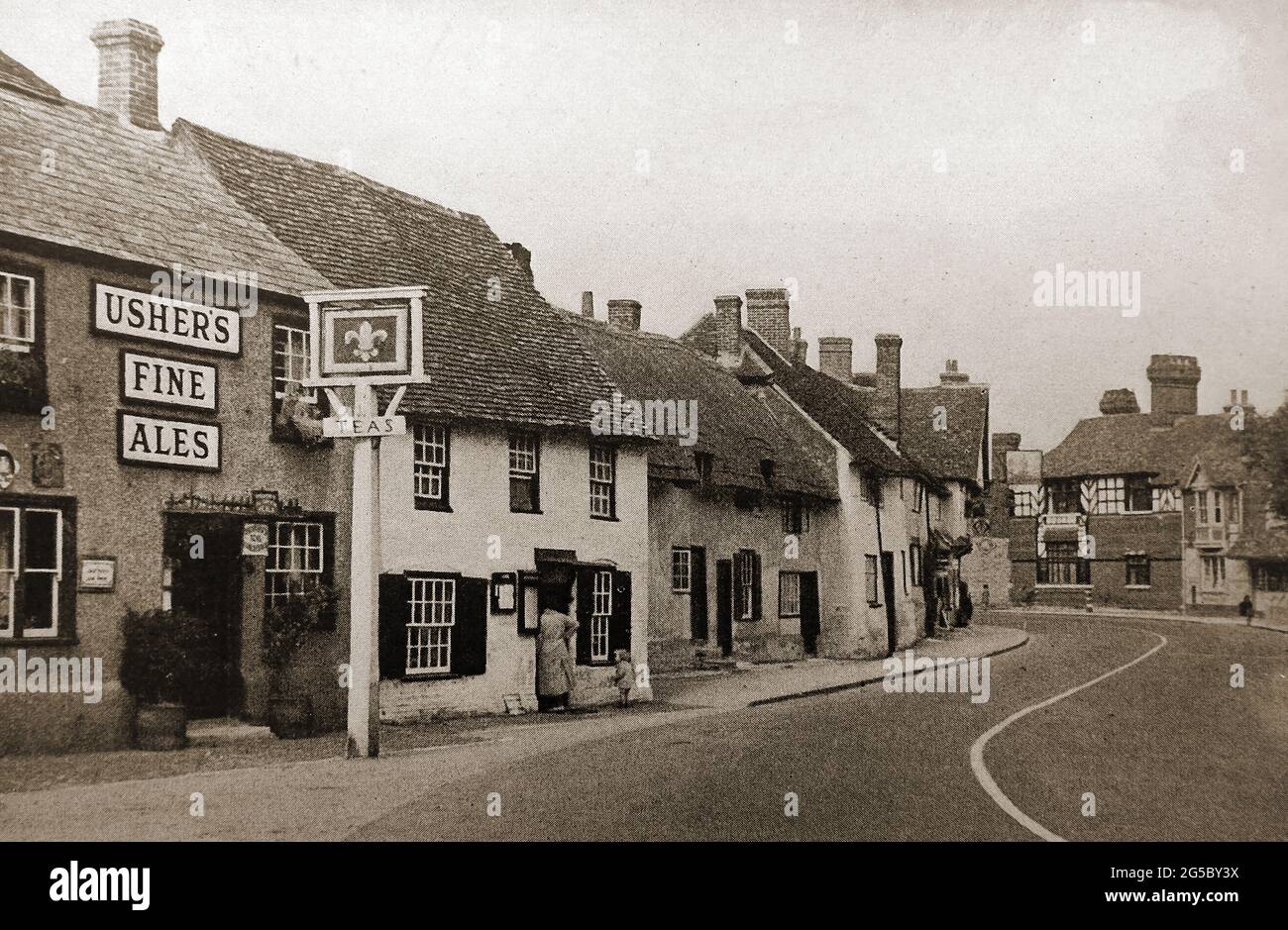 The Fleur de Lys,  ( An Ushers Brewery pub), Dorchester on Thames, Oxfordshire, UK circa 1930's /1940's with its inn sign and nearby thatched roof houses. Stock Photo