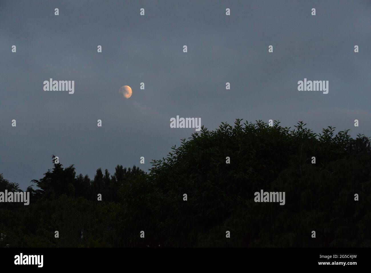 A full moon with a backdrop of heavy dark cloud at dawn in June 2021 in the UK. Stock Photo