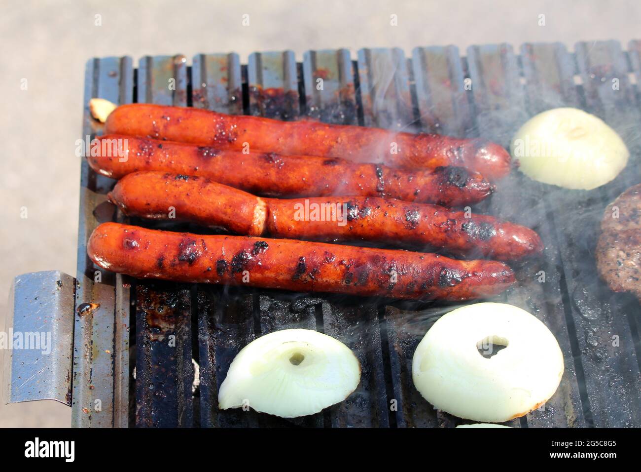 Well done sausages grilling on the edge of outside charcoal barbeque grill surrounded with smoke