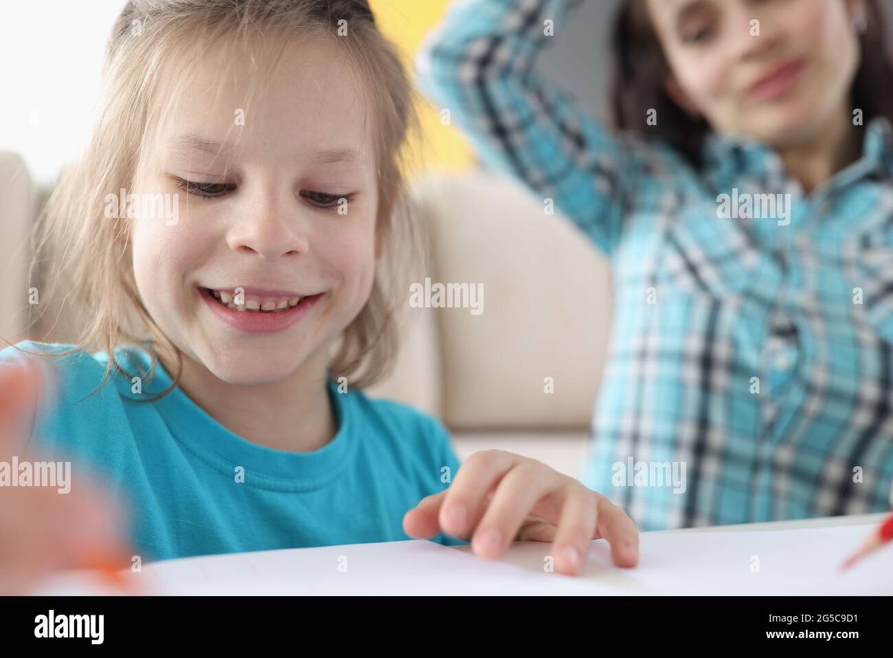 Little girl draws on paper next to mother Stock Photo Alamy