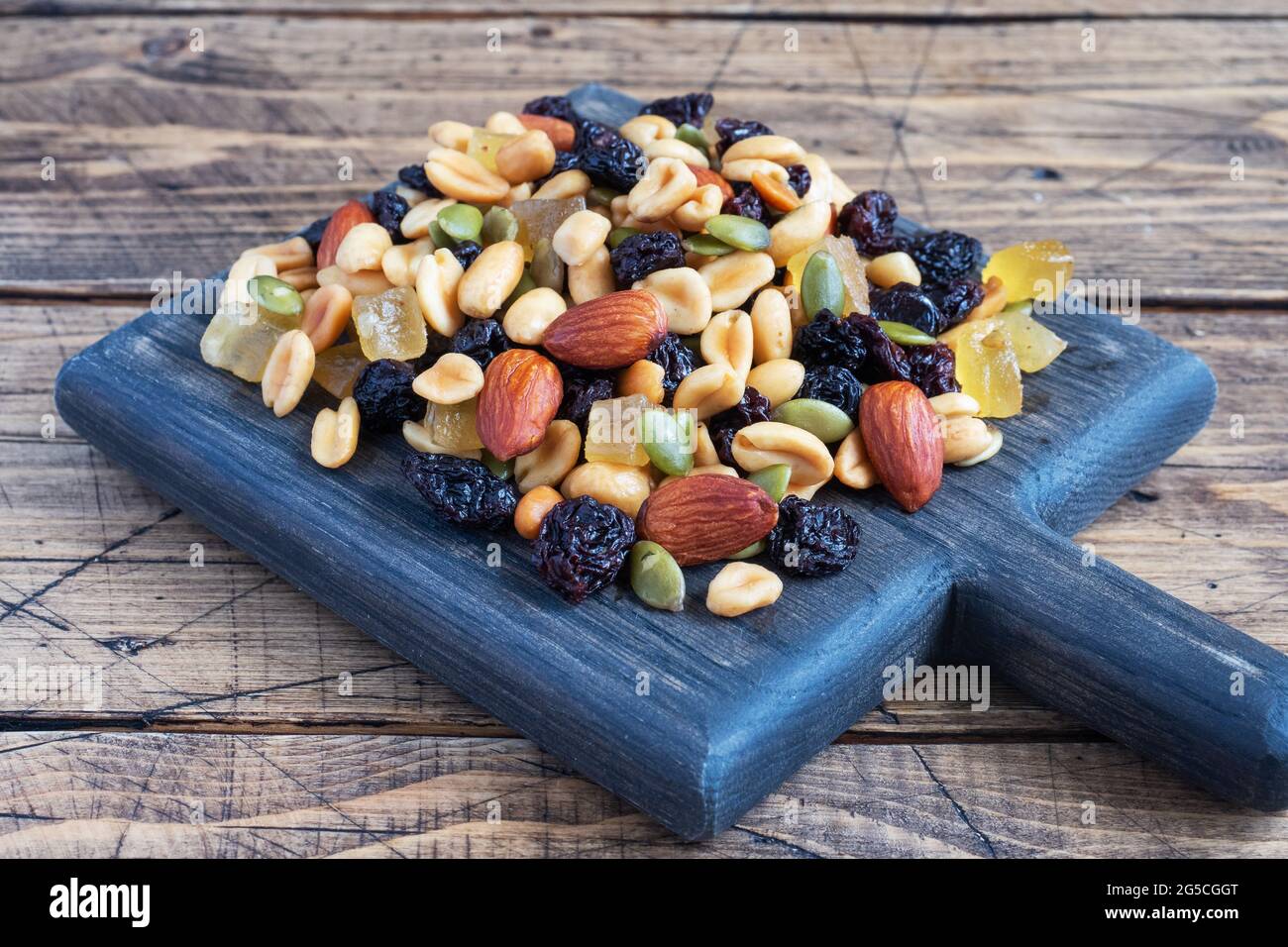 A mixture of nuts and dried fruits on a wooden chopping board, rustic background. Concept of healthy food Stock Photo