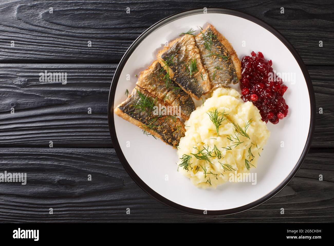 Fried herring fillets with mashed potatoes and lingonberry sauce close-up in a plate on the table. horizontal top view from above Stock Photo