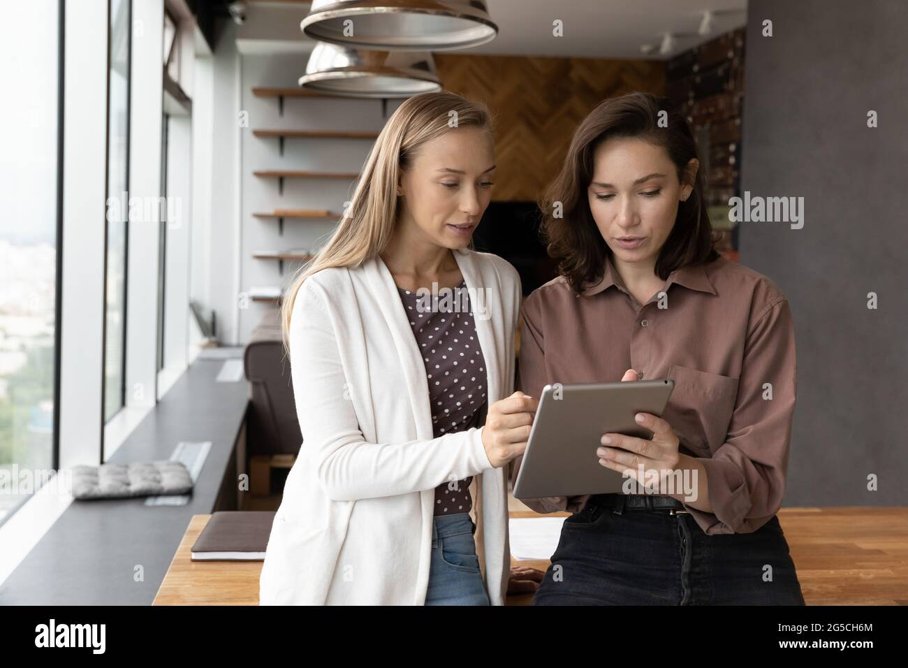 Focused two female colleagues working using digital tablet. Stock Photo