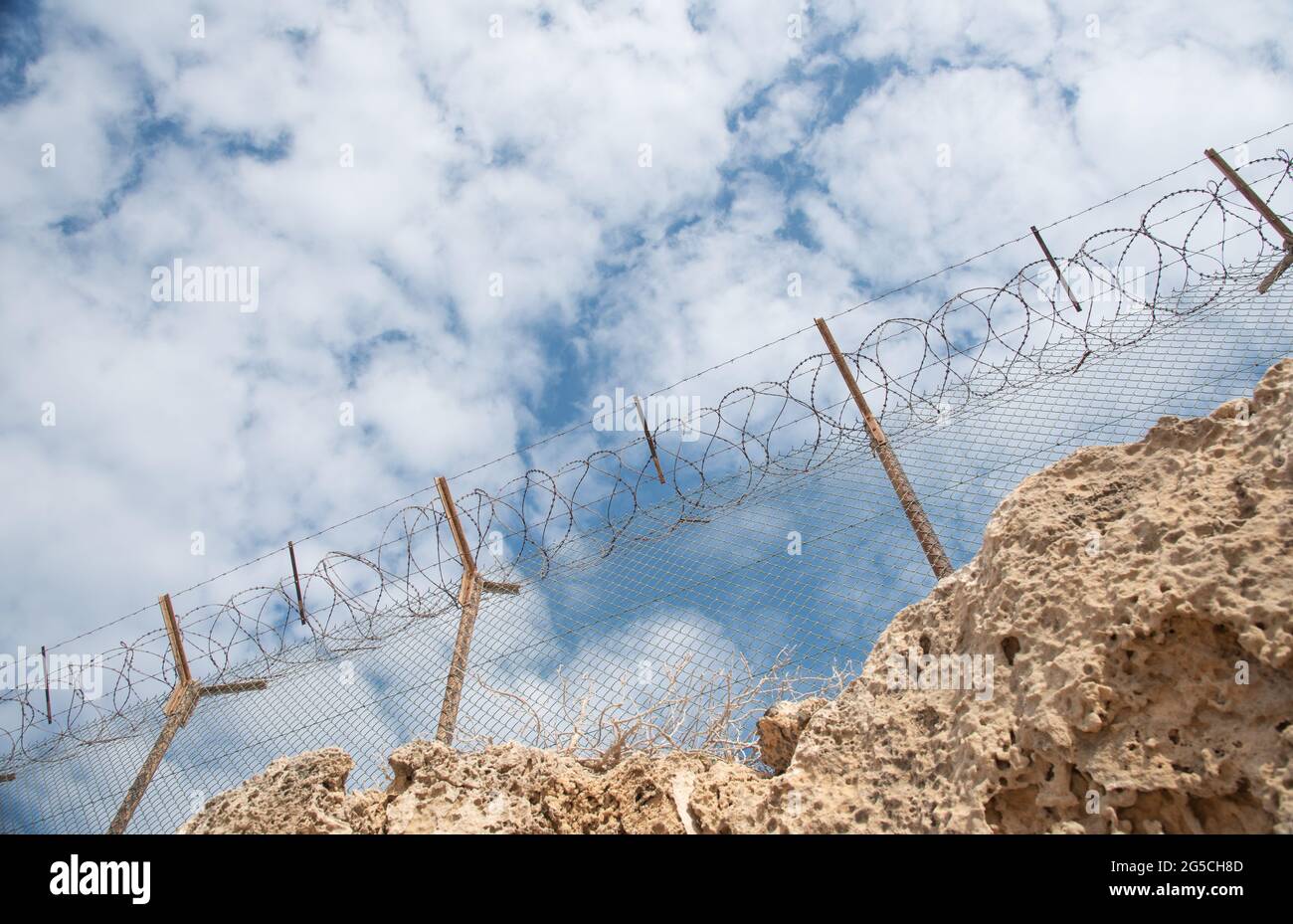 Security fence with barbed wire against a blue cloudy sky Stock Photo