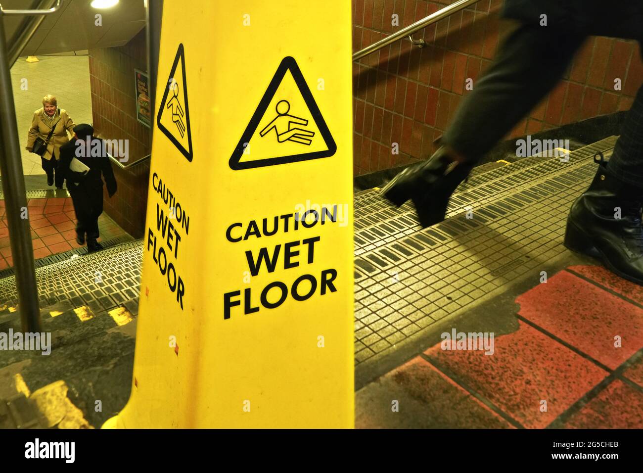 London, United Kingdom - February 01, 2019: Yellow cone with caution wet floor sign on stairs to underground station, passengers walking in background Stock Photo