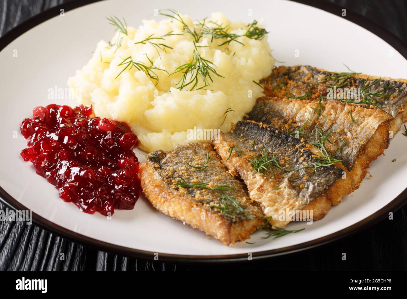 Fried herring fillets with mashed potatoes and lingonberry sauce close-up in a plate on the table. horizontal Stock Photo