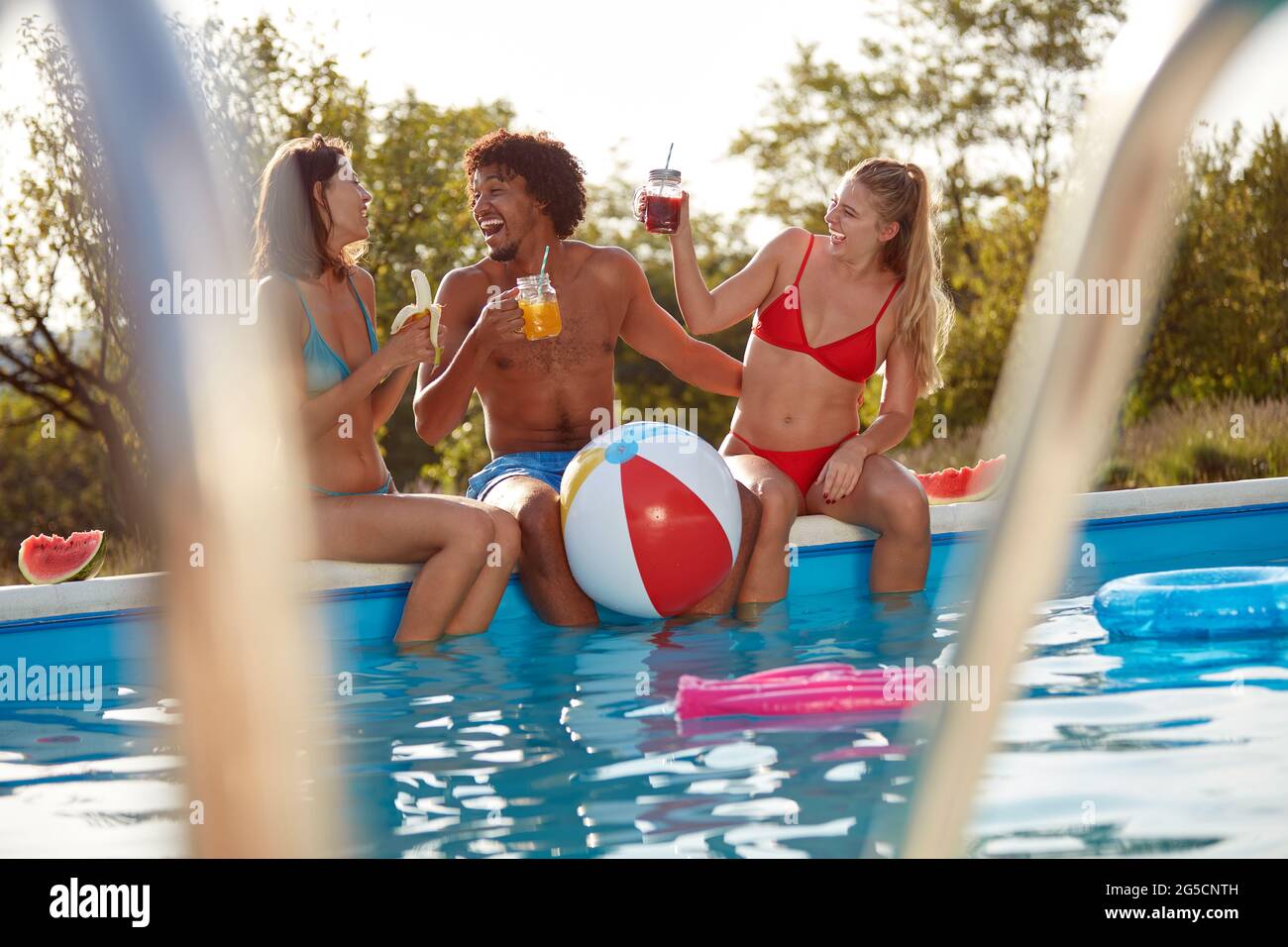 spontaneously  caught moment of afro-american young man having fun with two caucasian females outdoor in the nature by the pool Stock Photo