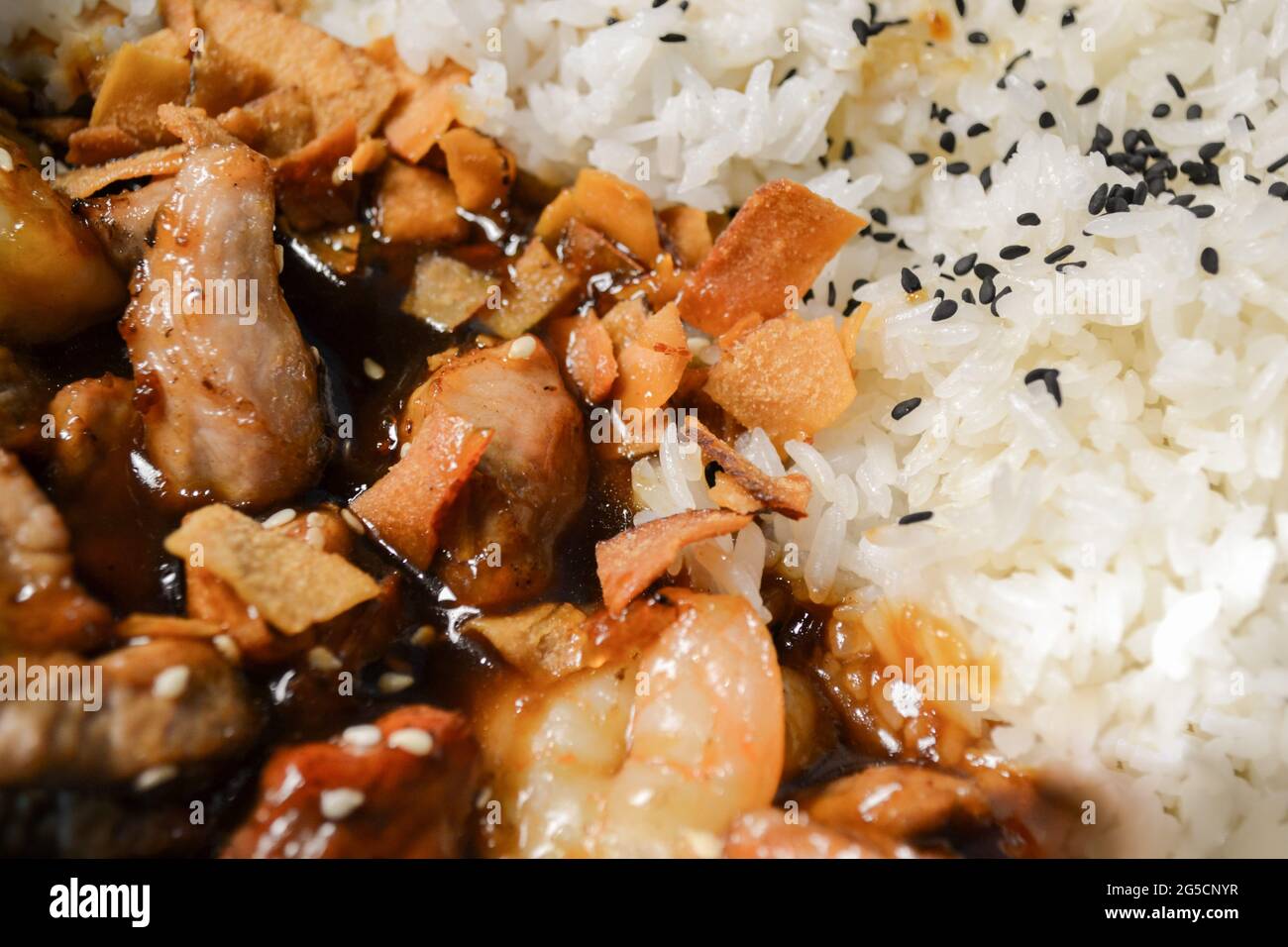 Close-up of Vietnamese food: rice sprinkled with black sesame seeds, beef in gravy, fried carrots. Stock Photo