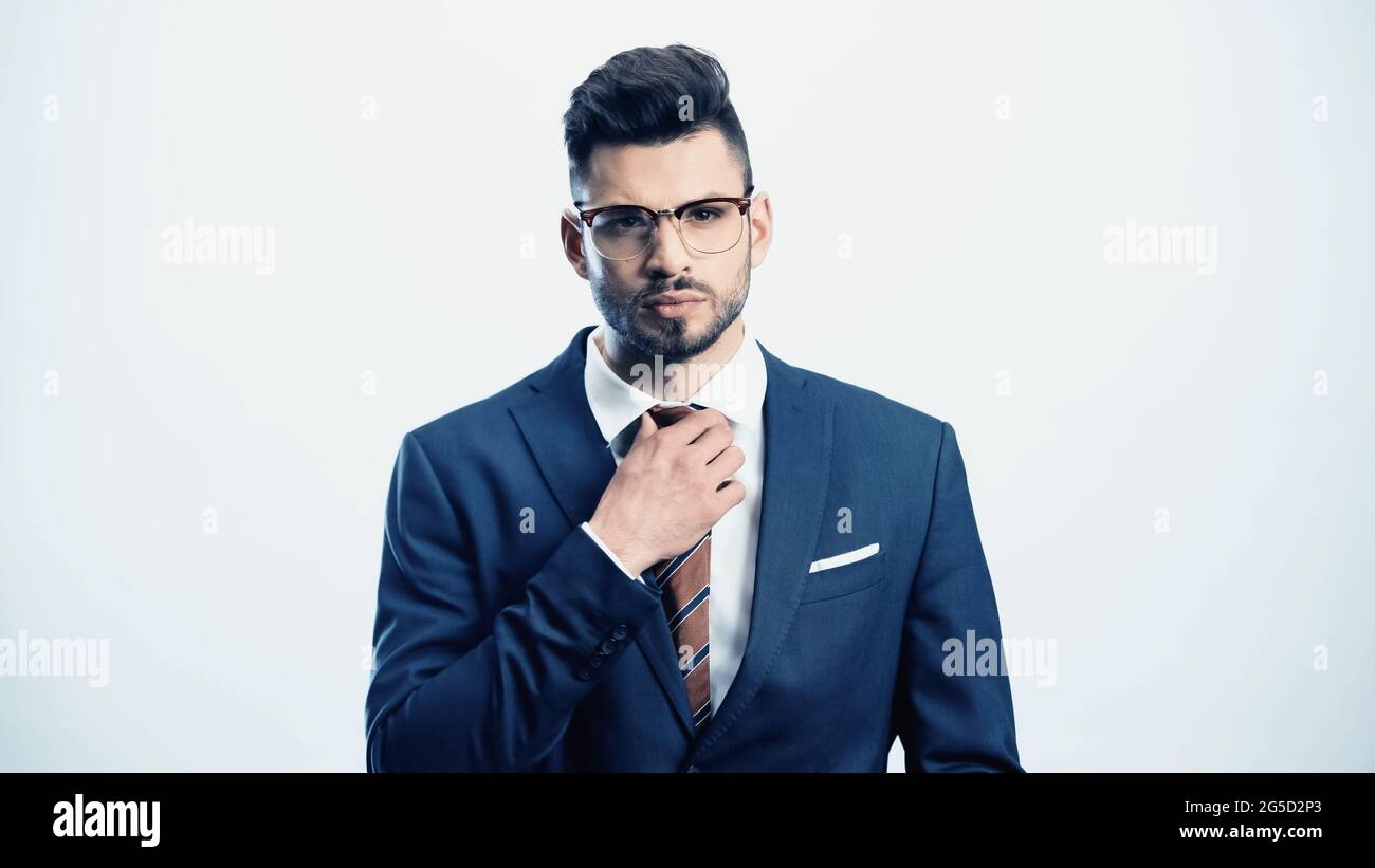 serious businessman touching tie while looking at camera isolated on white Stock Photo