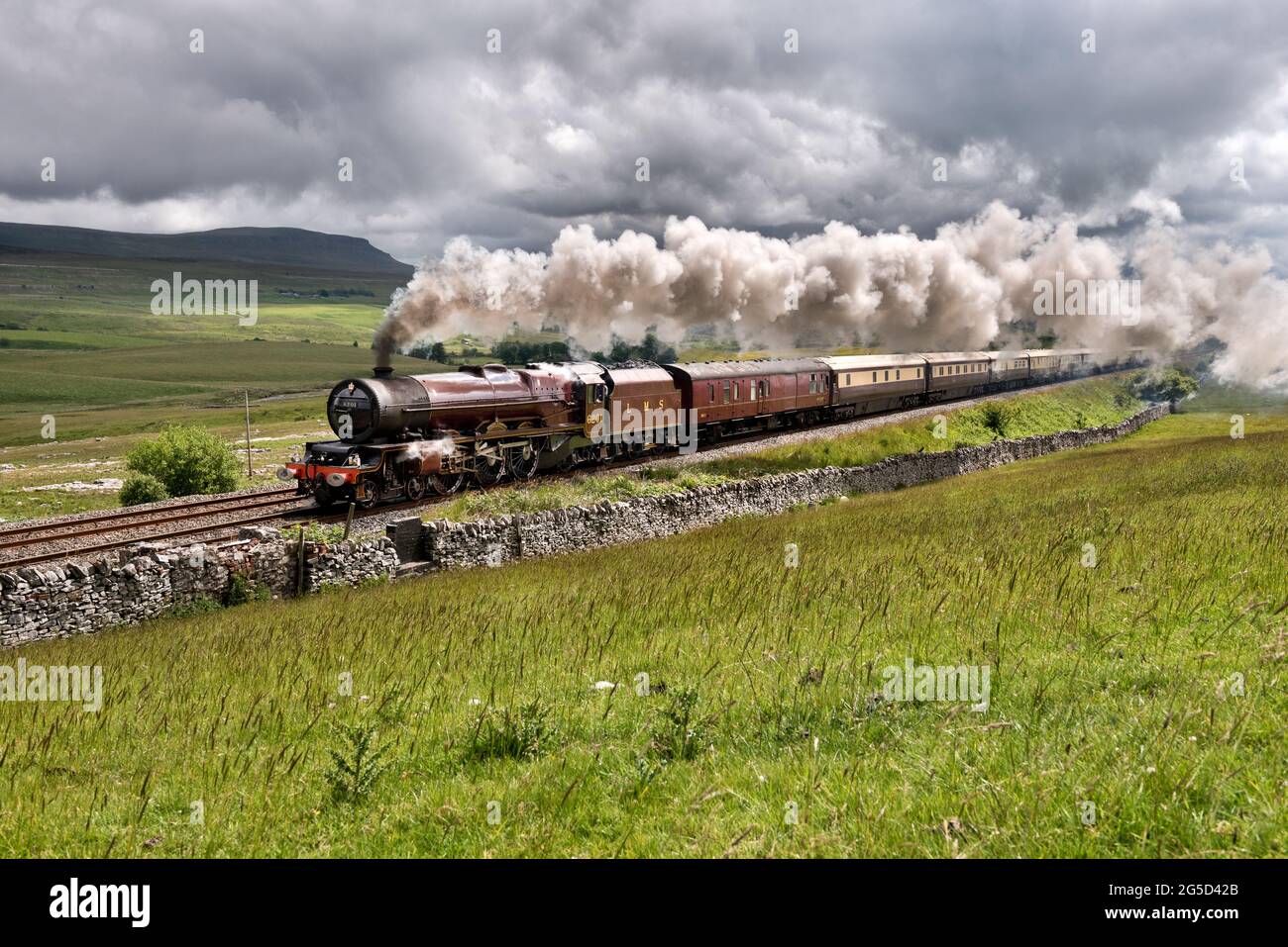 Ribblesdale, UK. 26th June, 2021. Set against a cloud-laden sky, steam locomotive Princess Elizabeth is seen in a patch of sunlight, with the Settle & Carlisle Steam Special, seen at Selside, Ribblesdale, in the Yorkshire Dales National Park. Pen-y-ghent peak is seen in teh background. The train ran from Coventry to Carlisle, with steam haulage from Preston to Carnforth. The outward journey was on the Settle-Carlisle line to Carlisle, returning via Shap. Credit: John Bentley/Alamy Live News Stock Photo