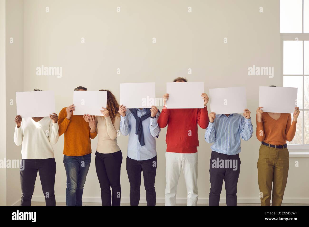 Group of people cover faces hiding behind white paper banners they are holding in hands Stock Photo