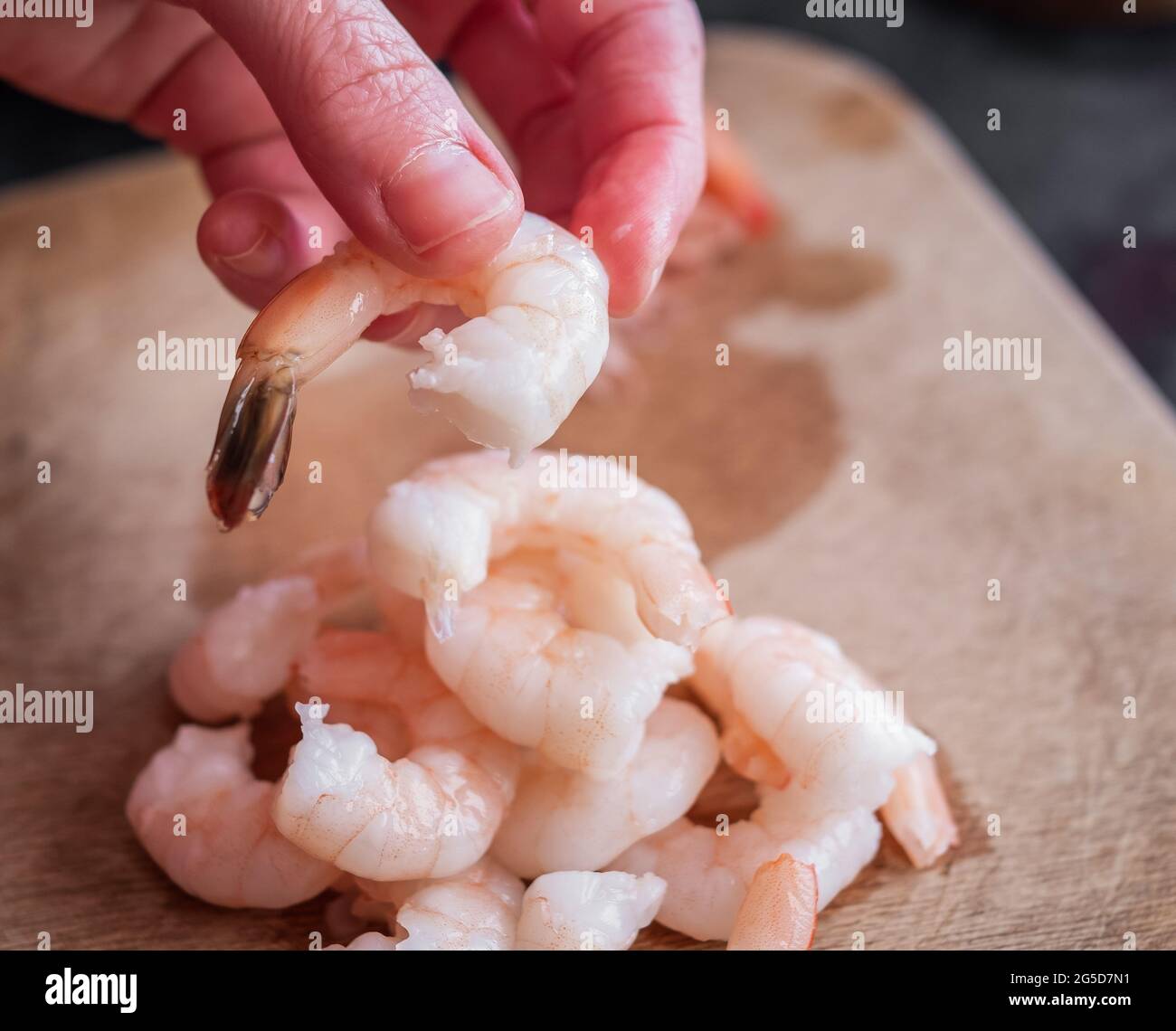 Undientifiable chef peeling the tails off raw king prawns to make a
