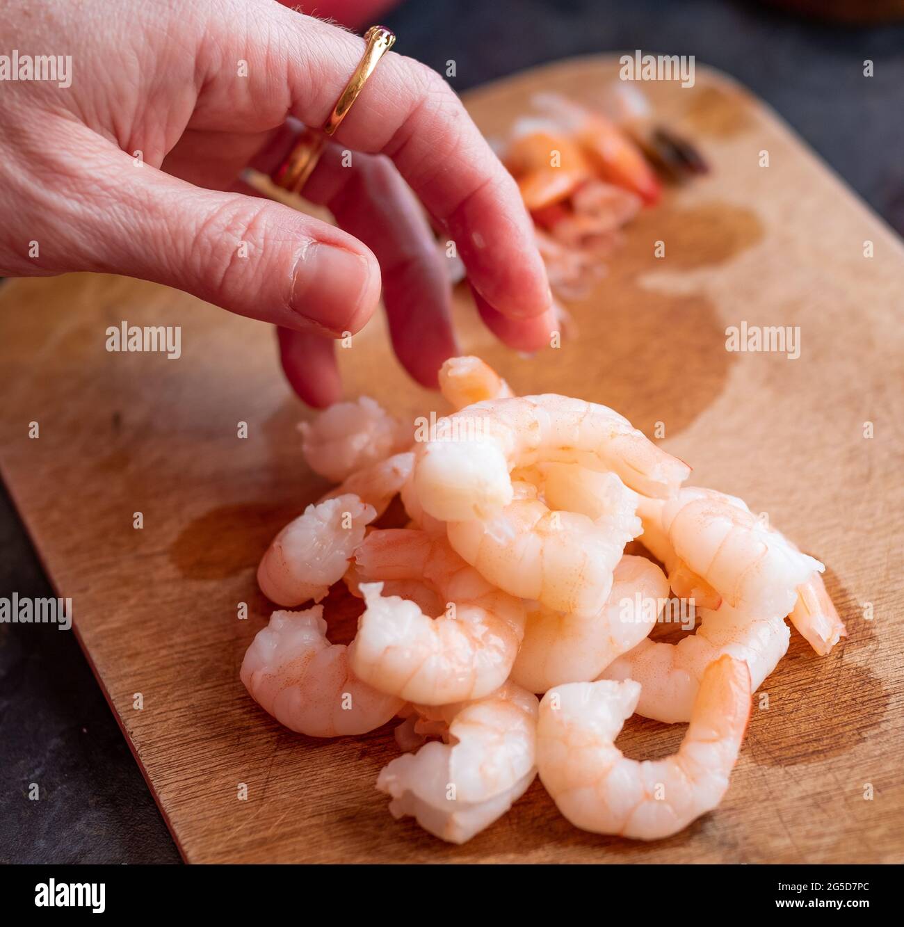 Undientifiable chef peeling the tails off raw king prawns to make a