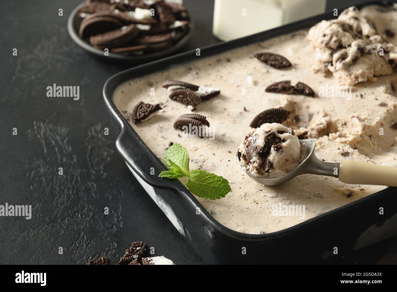 Homemade creamy ice cream with coffee cookies in container on a black background with copy space. Close up. Tasty children dessert without sugar. Stock Photo