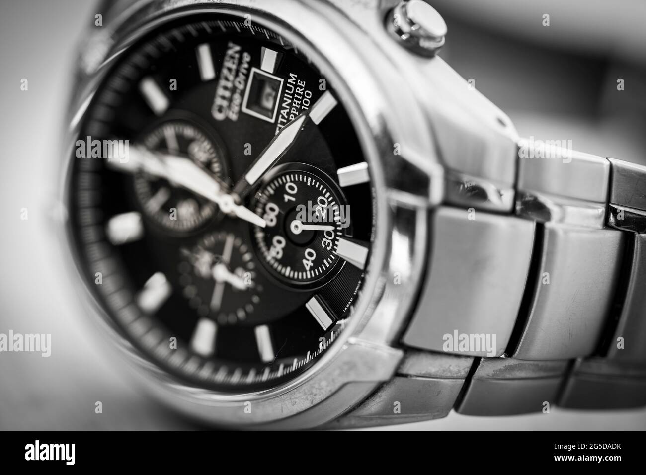 Monochrome black and white closeup image of a Citizen Eco Drive solar powered titanium metal man's wristwatch face showing clock hands and the strap Stock Photo