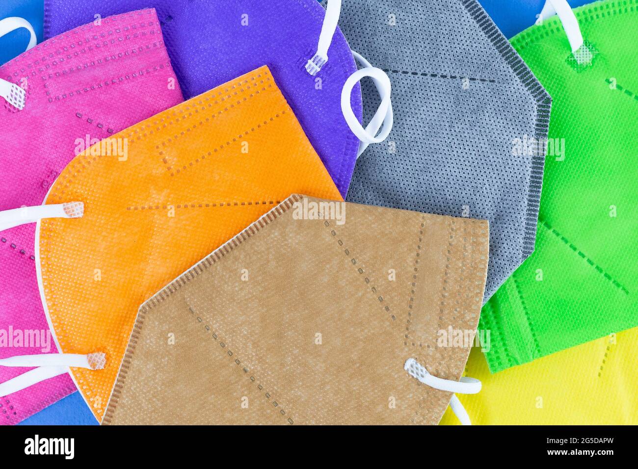 Heap of  different colors FFP2 or N95 face masks respirators on blue background. Top view flat layer. Protection from covid virus during pandemic. Stock Photo