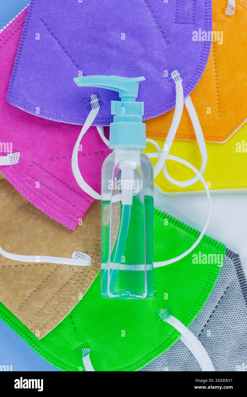 Hand alcohol sanitizer and different colors FFP2 or N95 face masks respirators heap. Top view flat layer. Protection from covid virus during pandemic. Stock Photo