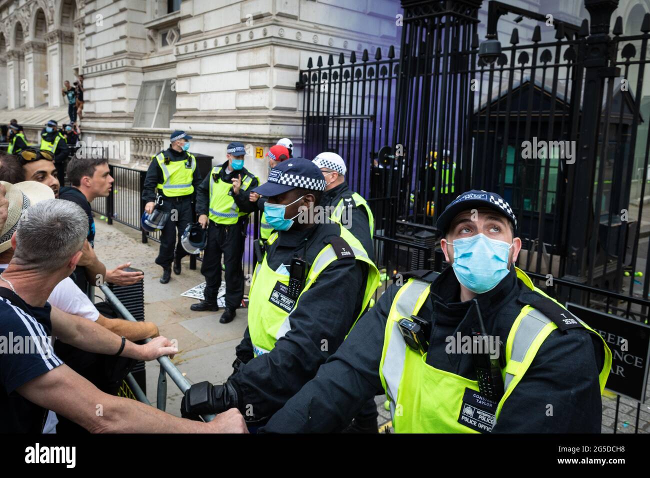 London, UK. 26th June, 2021. The police stand guard while protesters from an anti-lockdown demonstration throw tennis balls and smoke grenades into Downing street. Thousands of people marched to raise their concerns regarding government legislation centred around vaccinations and freedom to travel. Credit: Andy Barton/Alamy Live News Stock Photo
