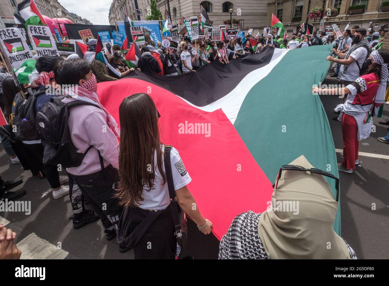 London, UK. 26th June 2021. People with giant Palestinian flag. Over five thousand joined the People's Assembly march through London against the failures of the Tory government during the pandemic, acting too late, handing out contracts to cronies and failing to reward key workers for their sacrifices. They demanded a 'new normal' with an end to NHS privatisation, decent housing, real action over climate change, decent housing, an end to unfair employment practices and the sacking of corrupt politicians. Peter Marshall/Alamy Live News Stock Photo