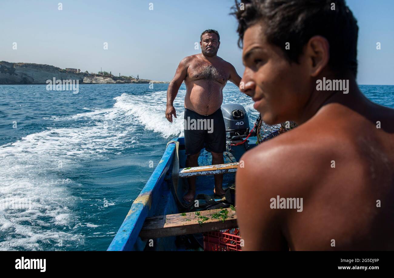 June 26, 2021, Beirut, Beirut, Lebanon: Fishermen Mohammad Itani pilots the boat while his son, Moustapha Itani, looks to land while they fish the Mediterranean Sea near the Rock of RaouchÅ½, Beirut, Lebanon on June 26, 2021. Fishermen use to get paid LL10,000 for each kilogram (2.2 pounds) of fish when the Lebanese Lira traded at LL1,500 per $1. Today, the LiraÃs value hit a record low, trading at least at LL18,000, yet the fishermen get paid LL25,000 per kilogram of fish. Their diminished wages make boat upkeep difficult so some fishers, unable to pay for repairs, send their boats to the ju Stock Photo