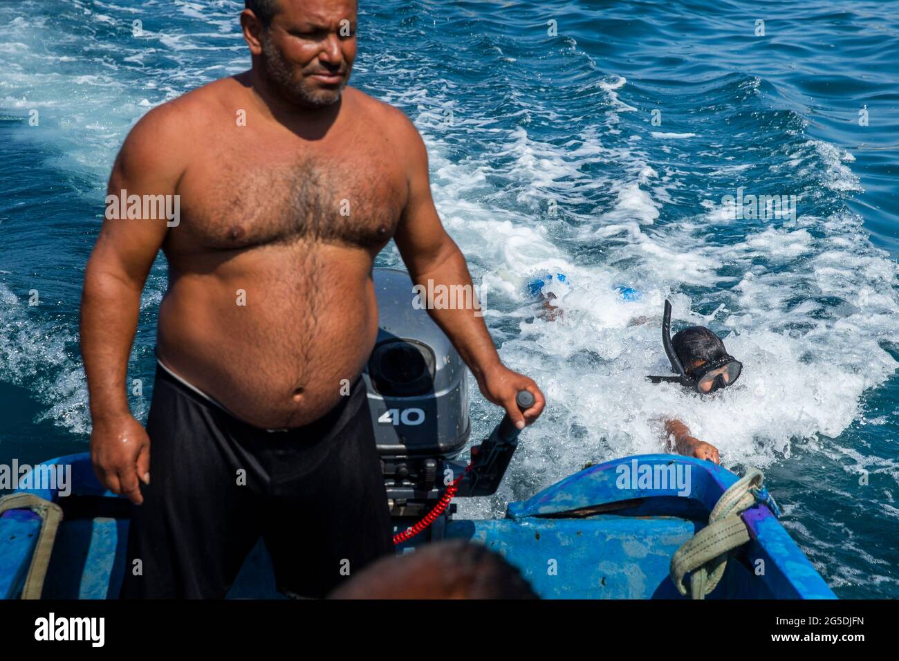 June 26, 2021, Beirut, Beirut, Lebanon: Fisherman Mohammad Itani pilots the boat while his son, Moustapha Itani, gets towed as they move to the submerged cages they are using to catch fish in the Mediterranean Sea near the Rock of RaouchÅ½, Beirut, Lebanon on June 26, 2021. Fishermen use to get paid LL10,000 for each kilogram (2.2 pounds) of fish when the Lebanese Lira traded at LL1,500 per $1. Today, the LiraÃs value hit a record low, trading at least at LL18,000, yet the fishermen get paid LL25,000 per kilogram of fish. Their diminished wages make boat upkeep difficult so some fishers, unab Stock Photo