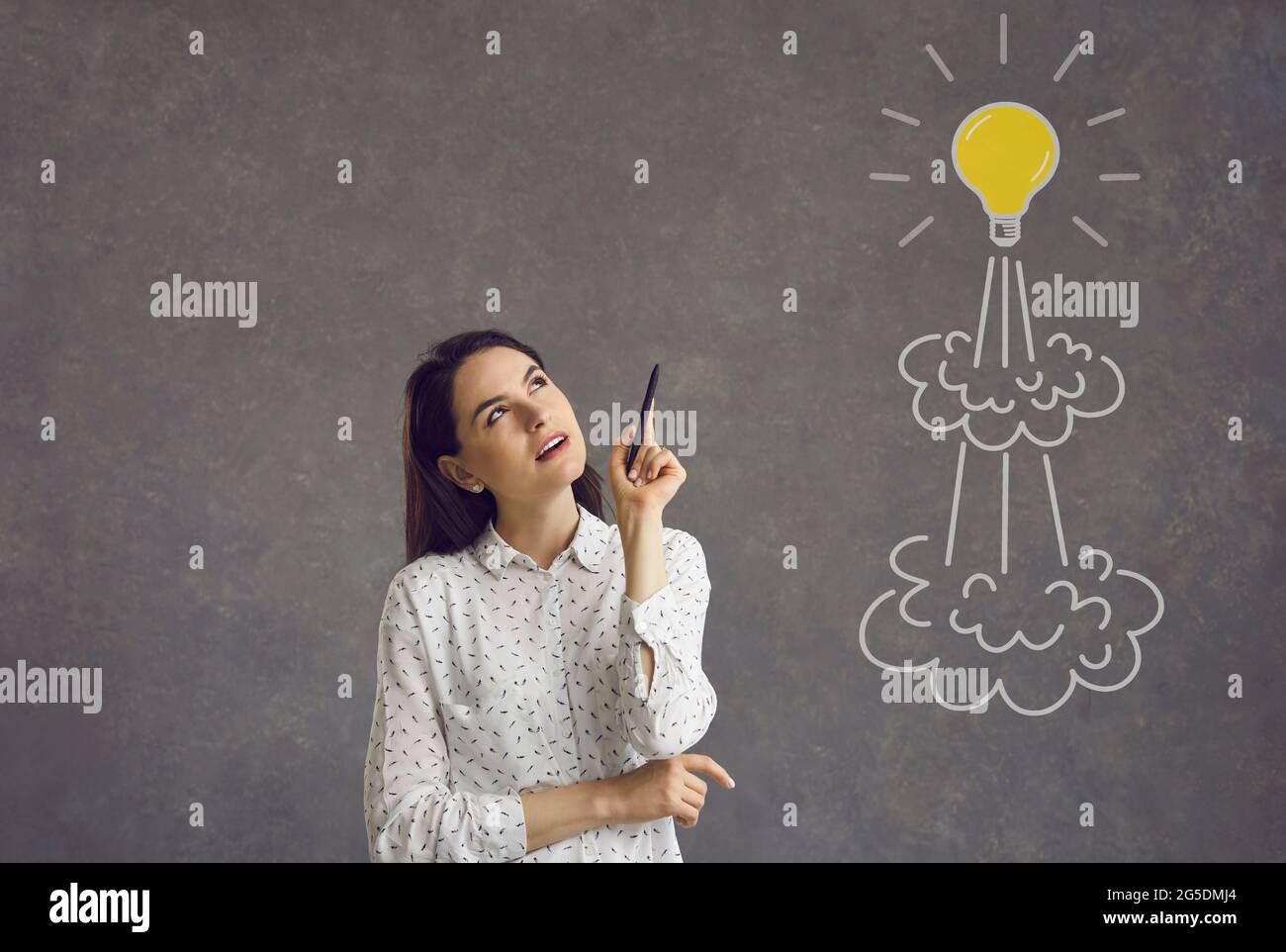 Woman with pen looking at flying light bulb rocket and thinking of her own business startup idea Stock Photo