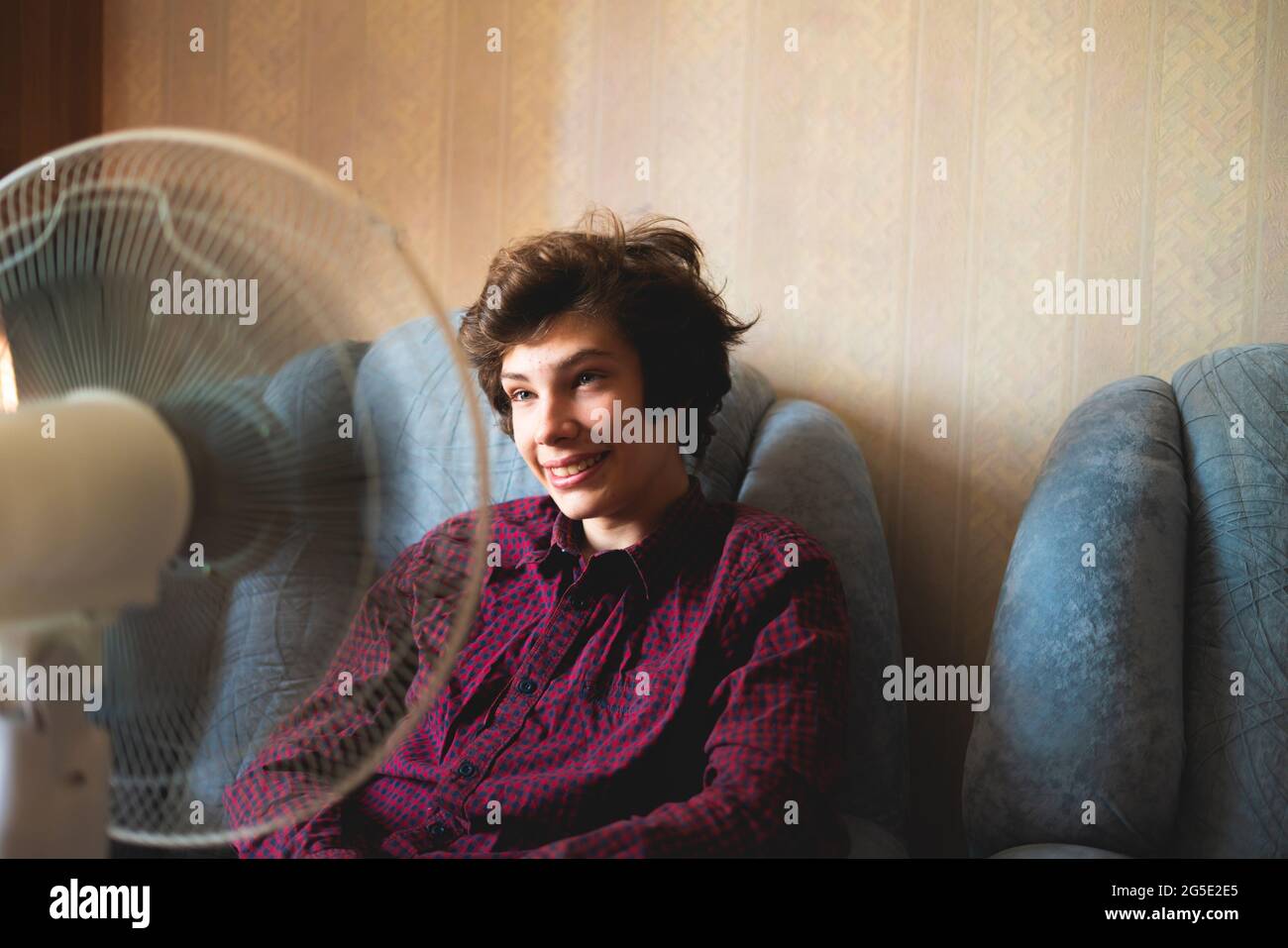 person enjoying the electric fan, cooling his face at home, during ...
