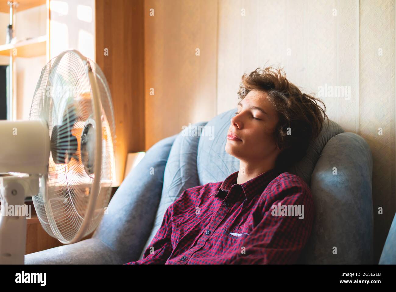 person enjoying the electric fan, cooling his face at home, during ...
