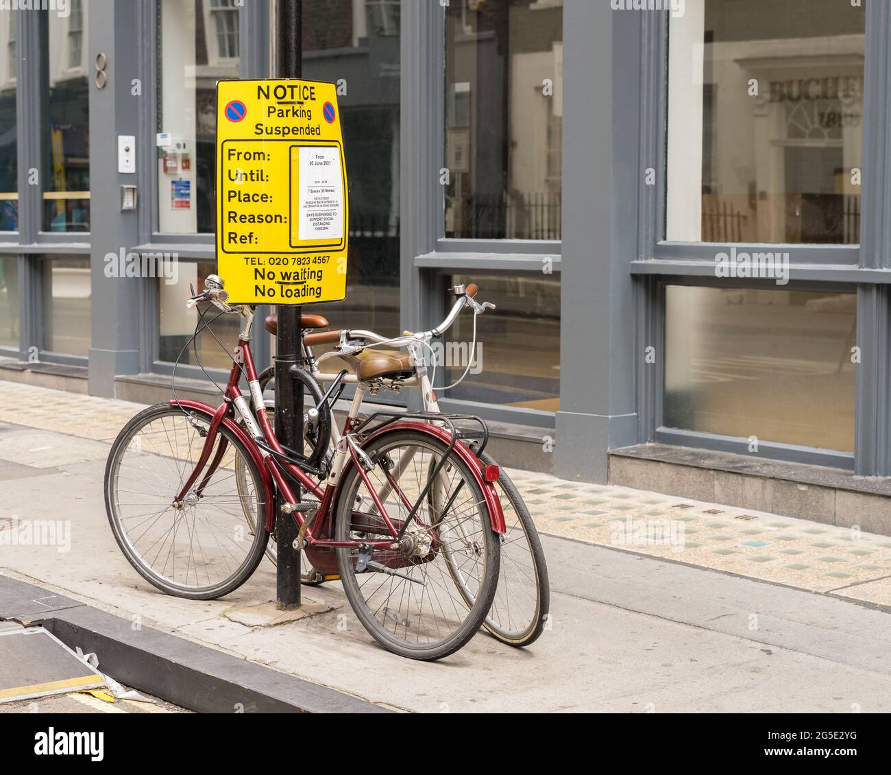 Parking suspended sign on a lamppost with two bicycles chained up underneath. London - 26th June 2021 Stock Photo
