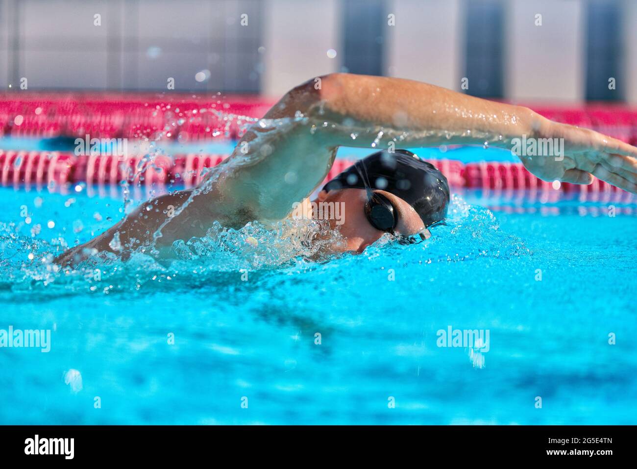 Swimmer man doing crawl swim in swimming pool portrait. Closeup of athlete wearing goggles, swimming cap training in blue water indoors Stock Photo