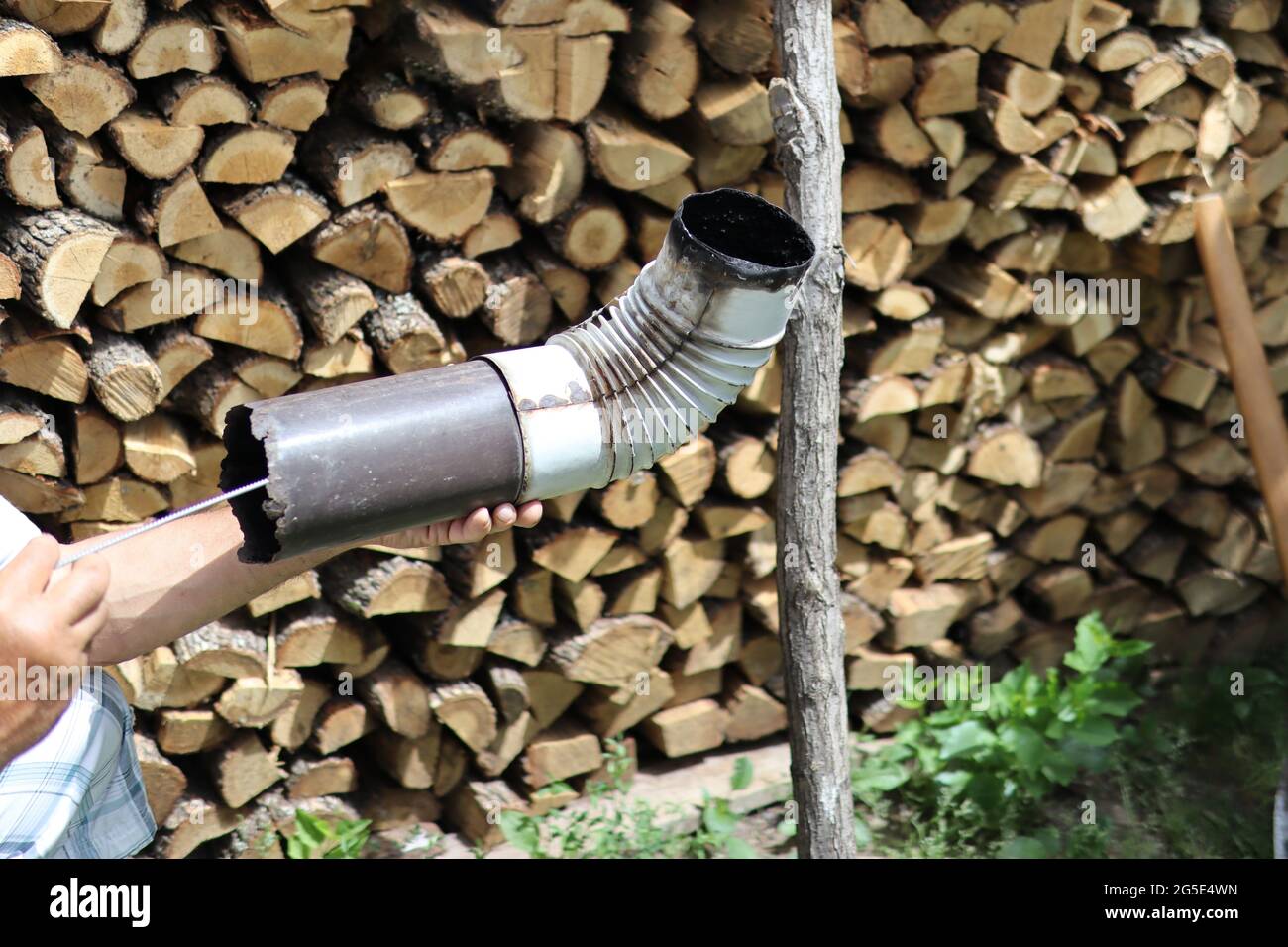 Man cleaning chimney pipe outside with tool. Cleaning a wood burning stove concept. Close up, and wood log in blurred background Stock Photo